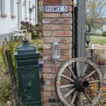 Brama Siedliska Dobrych Snów w Płowcach na Mazurach z ceglanym słupkiem, starą skrzynką pocztową i drewnianym kołem.