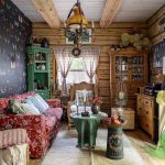 Przytulny salon w drewnianym domu z czerwoną sofą, tapetą w motyle, wiklinowymi meblami i rustykalnymi dekoracjami.