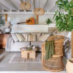 Salon w greckim domu z jasną sofą, wiklinowym fotelem, drewnianym stolikiem i dużą rośliną w ceramicznej donicy.