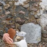 Detal starego kamiennego muru w mazurskim siedlisku z dekoracyjną kamienną płytą i koszem pełnym miękkich pledów.