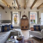Rustykalny salon w mazurskim siedlisku z jasną sofą, antyczną szafą, drewnianymi belkami i ceglanym podłogą.