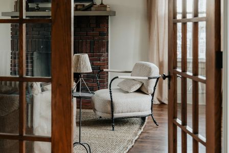 Przytulny salon inspirowany naturą z piecem wolnostojącym, dużymi oknami z widokiem na las, drewnianym stolikiem i meblami w ciepłych, naturalnych kolorach.