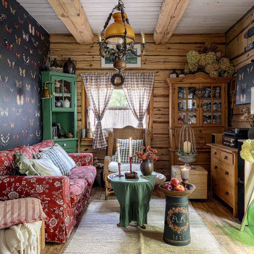 Przytulny salon w drewnianym domu z czerwoną sofą, tapetą w motyle, wiklinowymi meblami i rustykalnymi dekoracjami.