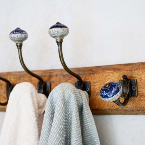 Drewniany wieszak ścienny z ceramicznymi gałkami i zawieszonymi ręcznikami w łazience w stylu rustykalnym.