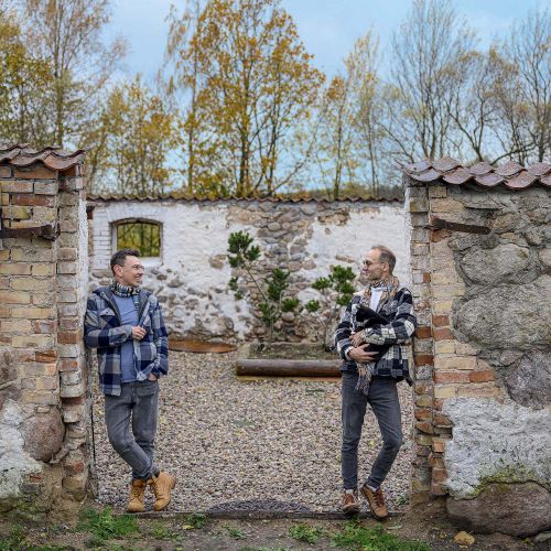 Łukasz i Arek stoją przy wejściu na patio swojego siedliska w Płowcach na Mazurach, w otoczeniu starych kamiennych murów.
