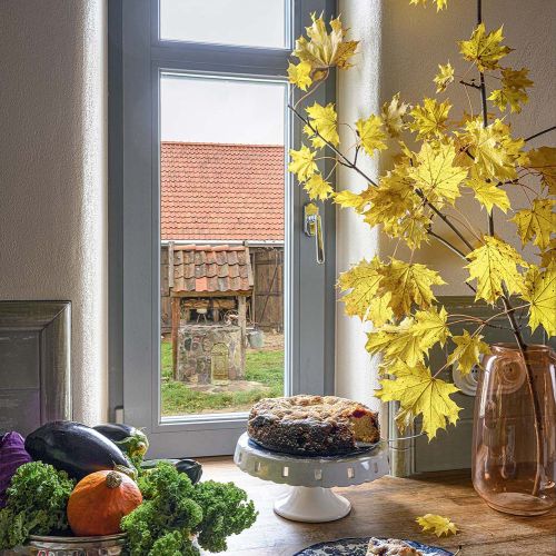 Jesienna aranżacja kuchennego blatu w domu na Mazurach z ciastem, owocami, warzywami i gałęziami żółtych klonowych liści.