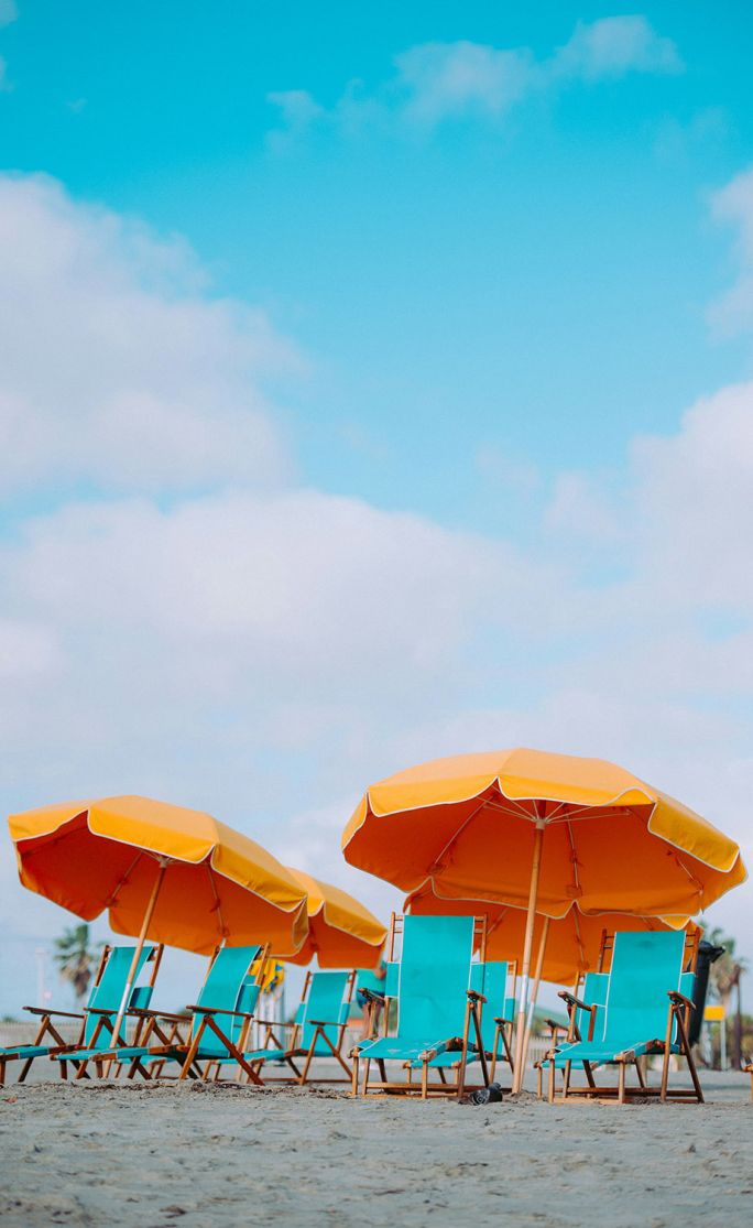 pomarańczowe parasole na plaży na tle turkusowego nieba