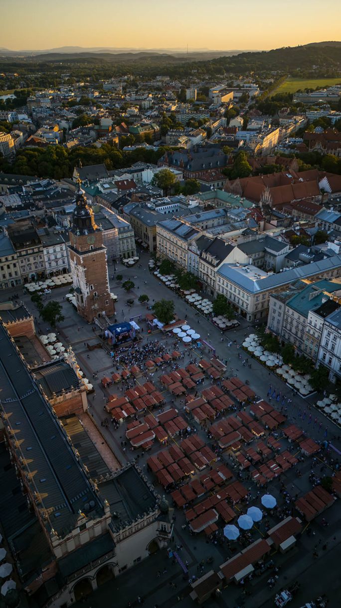 Widok z góry na Rynek Główny w Krakowie z Sukiennicami, Wieżą Ratuszową i stoiskami targów sztuki ludowej o zachodzie słońca.