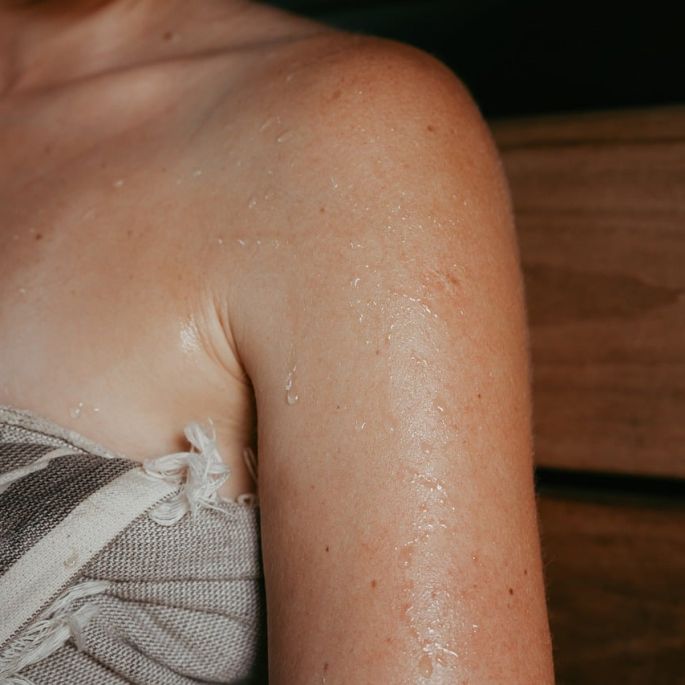 Drewniana sauna z piecem opalanym drewnem, ławami i dużym panoramicznym oknem wychodzącym na las. Naturalne drewno, ogień w palenisku i widok drzew tworzą spokojny, bliski naturze klimat.