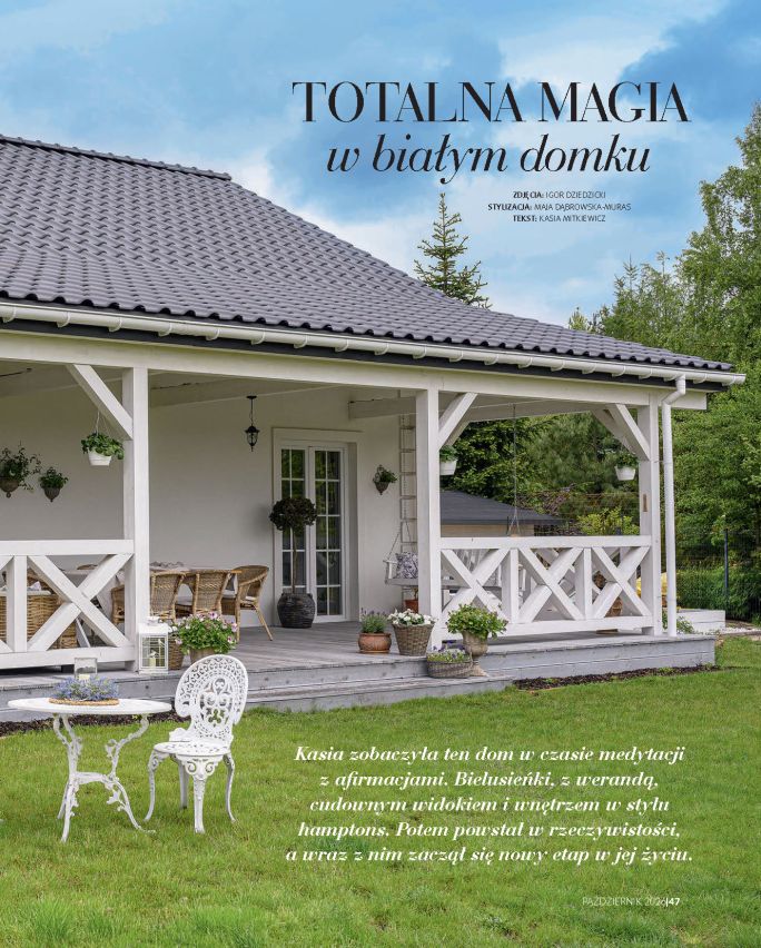Biały dom z przestronną werandą w stylu hamptons, otoczony zielonym ogrodem i dekoracyjnymi donicami z kwiatami.