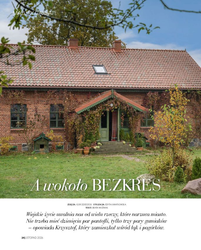 Stary ceglany dom na Mazurach Garbatych, z zieloną stolarką i gankiem porośniętym pnączami, otoczony jesiennym ogrodem. Na stronie otwierającej reportaż widnieje tytuł „A wokoło bezkres”.