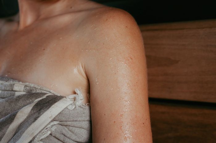 Drewniana sauna z piecem opalanym drewnem, ławami i dużym panoramicznym oknem wychodzącym na las. Naturalne drewno, ogień w palenisku i widok drzew tworzą spokojny, bliski naturze klimat.