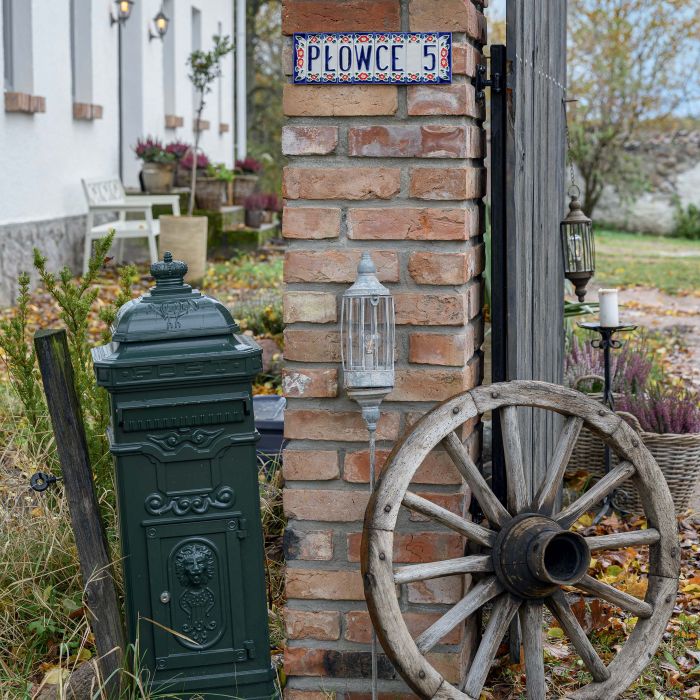 Biały wiejski dom z czerwonym, ceramicznym dachem i szarymi oknami, otoczony starymi drzewami i jesiennym ogrodem.