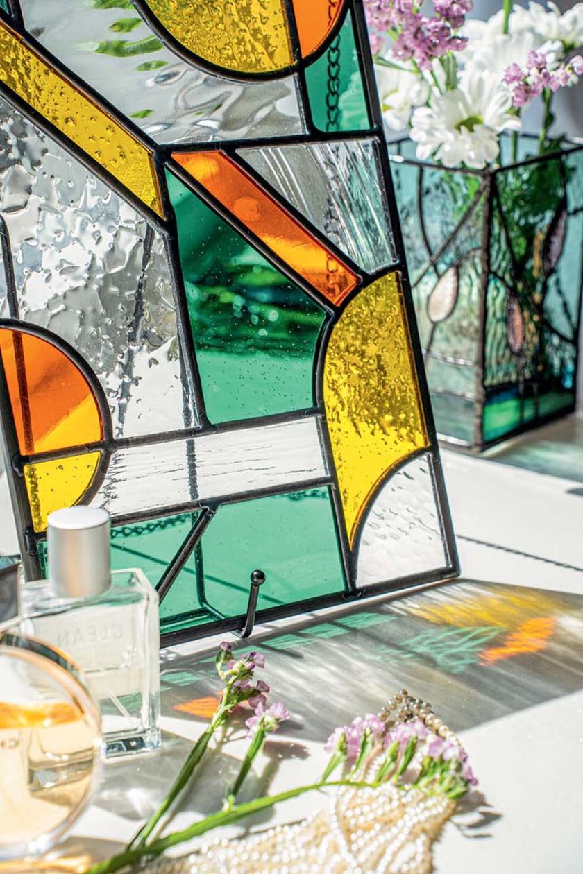 Dekoracyjny witraż z zielonego, żółtego, pomarańczowego i przezroczystego szkła w słonecznym wnętrzu.