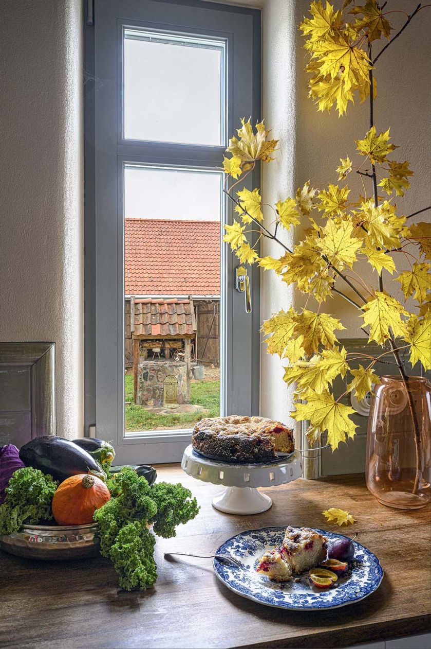 Jesienna aranżacja kuchennego blatu w domu na Mazurach z ciastem, owocami, warzywami i gałęziami żółtych klonowych liści.