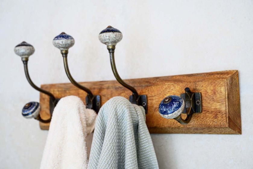 Drewniany wieszak ścienny z ceramicznymi gałkami i zawieszonymi ręcznikami w łazience w stylu rustykalnym.