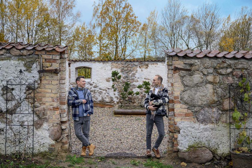 Łukasz i Arek stoją przy wejściu na patio swojego siedliska w Płowcach na Mazurach, w otoczeniu starych kamiennych murów.